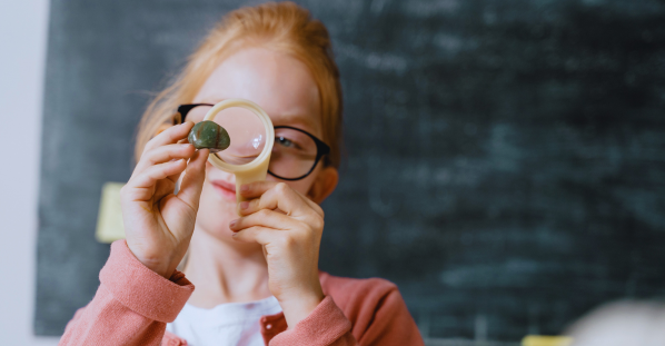 young girl in glasses views stone through magnifier