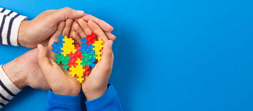 two hands hold heart displaying colours in support of autism spectrum disorder